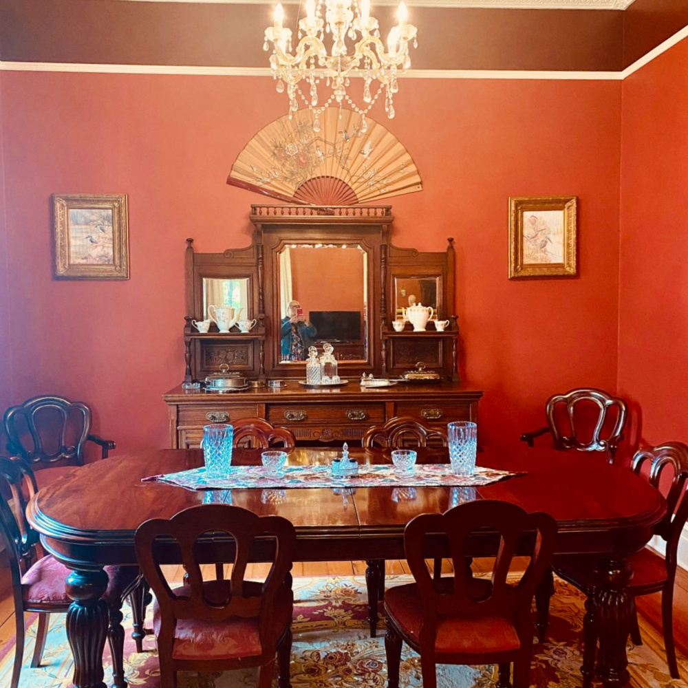 A period home in an old cottage with deep red walls, a chandelier and large oak table with six chairs
