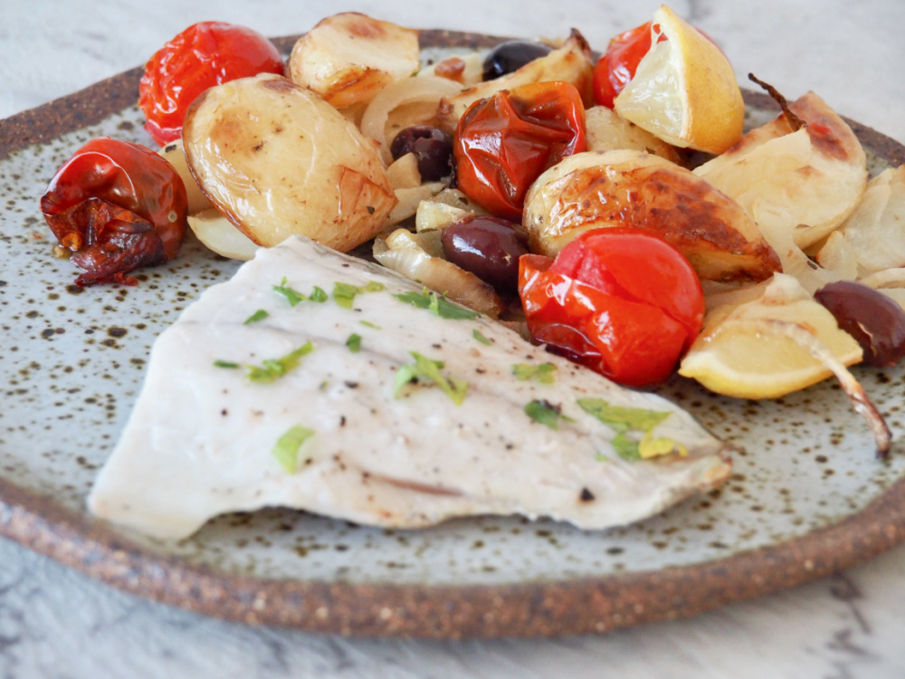 white fish fillet garnished with parsley and served with roast potatoes, tomatoes and sliced onions