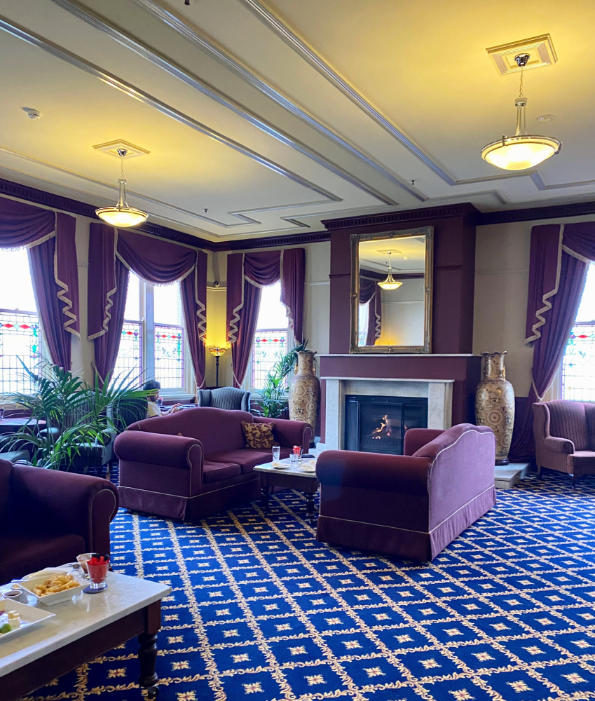 an old fashioned hotel lounge with big burgandy sofas and a roaring fire