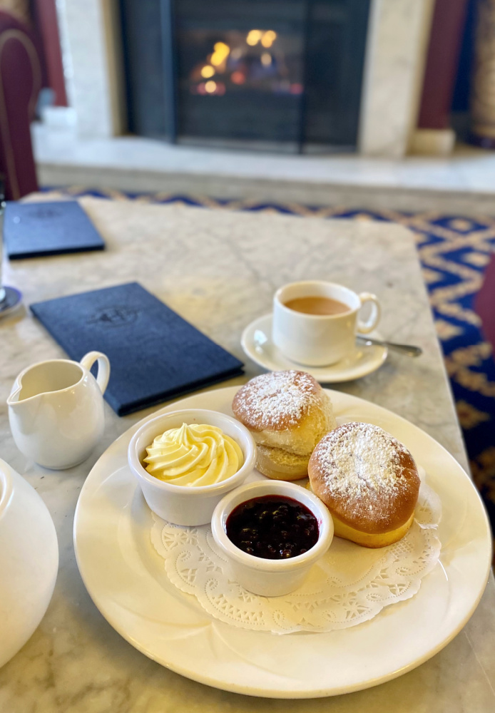 low marble table with cup of tea and a plate with 2 scones a pot of jam and a pot of cream