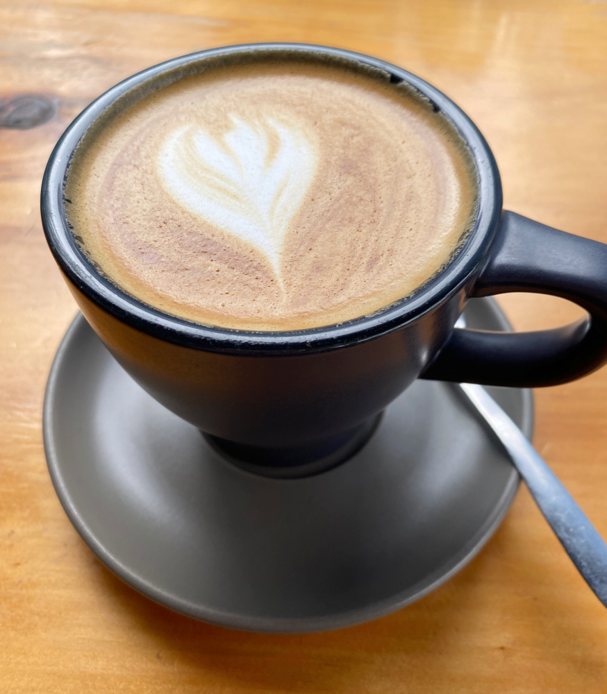 flat white coffee with heart shaped latte art in black cup with saucer