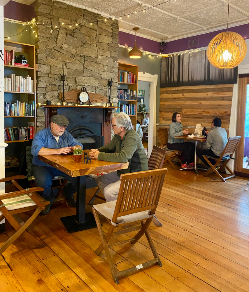 inside a cottage cafe with bookcases lining walls and a stone fireplace and a few people sitting at wooden tables