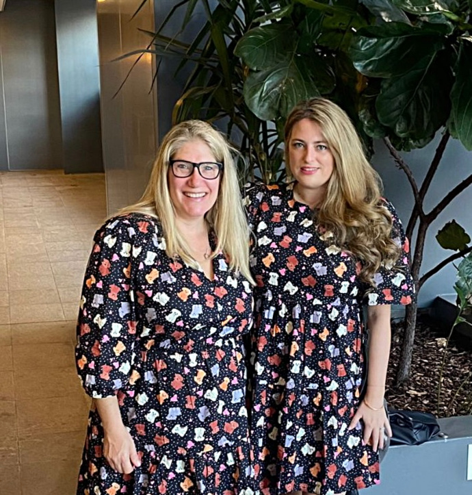 two women standing next to each other in matching dresses with puppies on