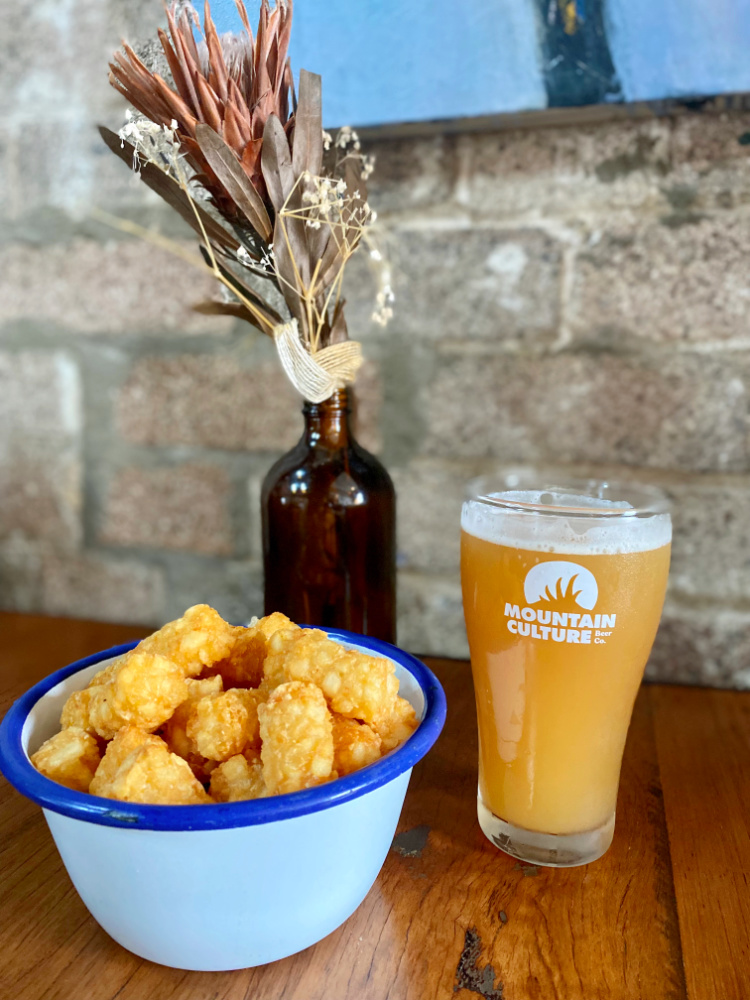 pint glass of mountain culture beer with a bowl of tater tots