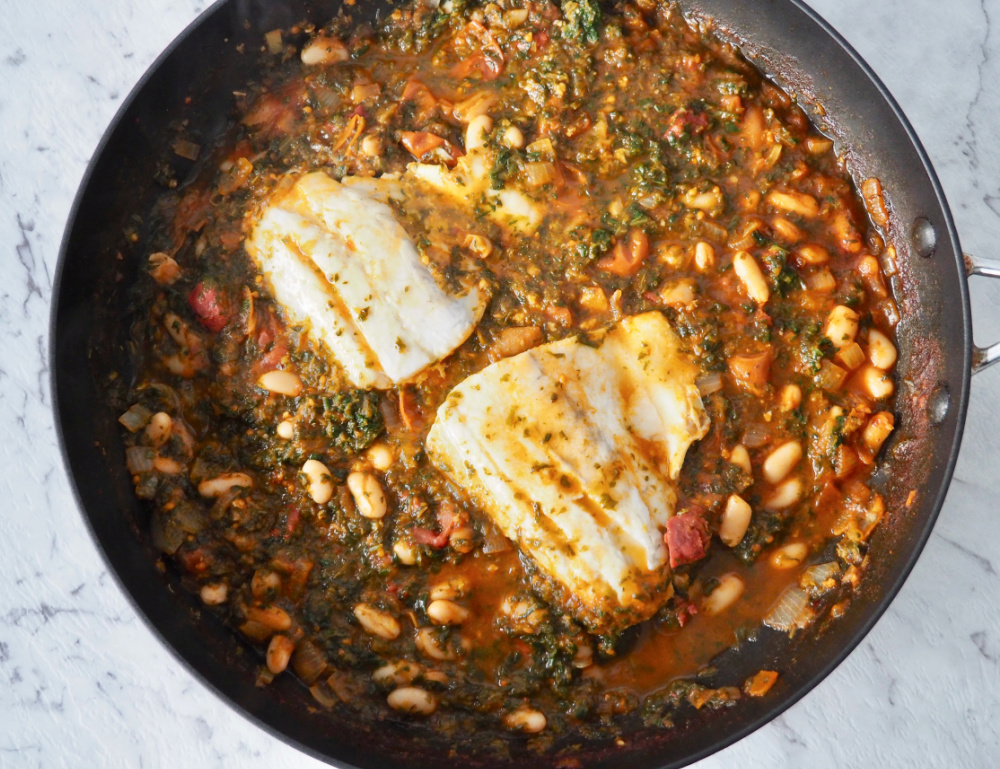 large frying pan with two fish fillets lying on a bed of spicy beans 