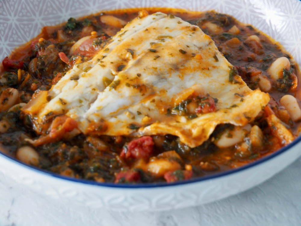 shallow dish with fish fillet lying on top of a bed of spicy beans