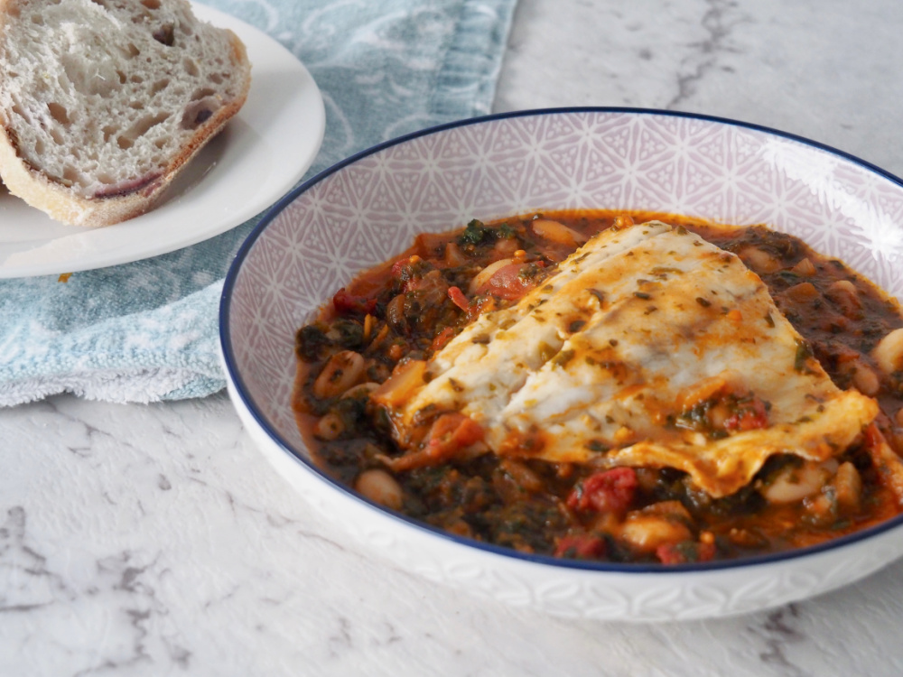 a shallow dish with a fish fillet lying on top of a bed of spicy beans