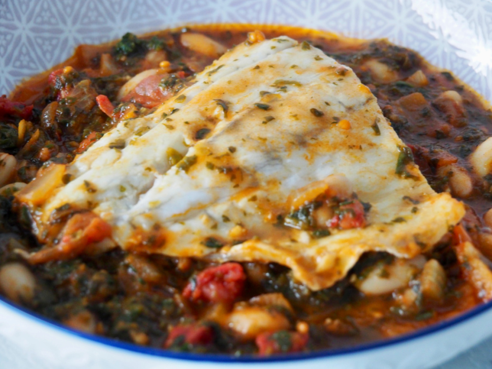 white fish fillet lying on top of a bed of spicy beans