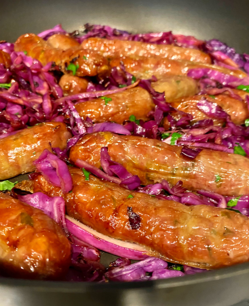 close up of pan with sausages nestled in bed of sliced red cabbage and garnished with parsley