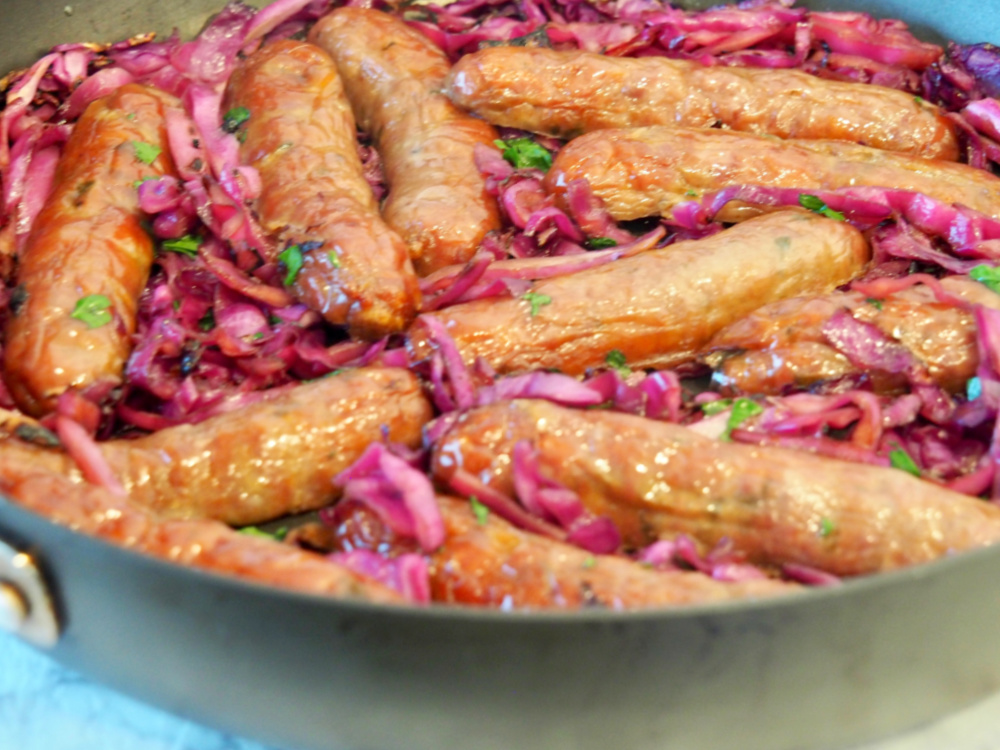 close up of pan with sausages nestled in sliced red cabbage garnished with parsley