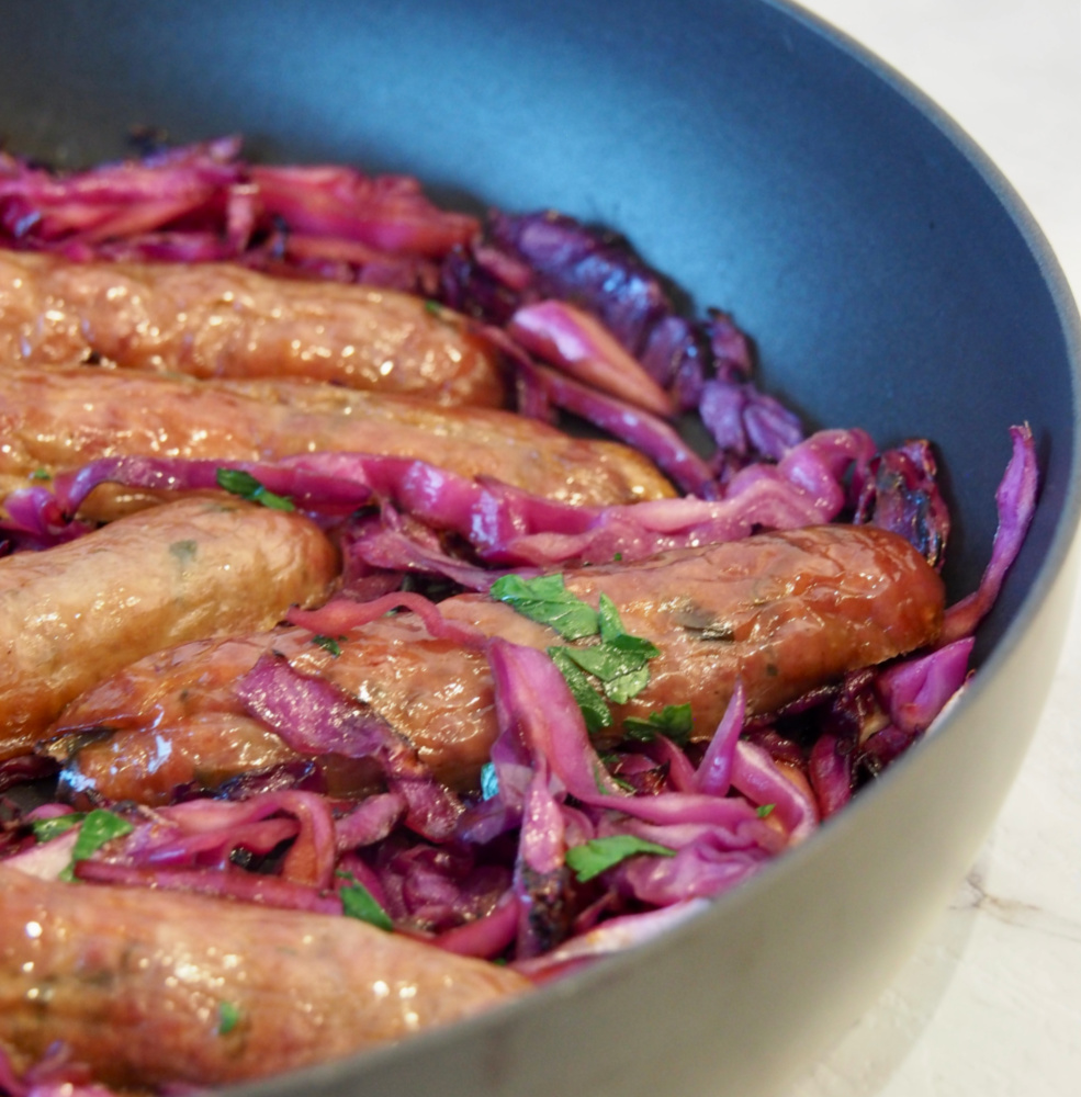 side view of pan with sausages nestled in sliced red cabbage garnished with parsley