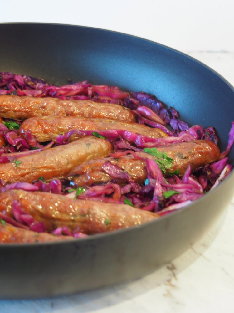 side view of pan with sausages lying on bed of sliced red cabbage and garnished with parsley