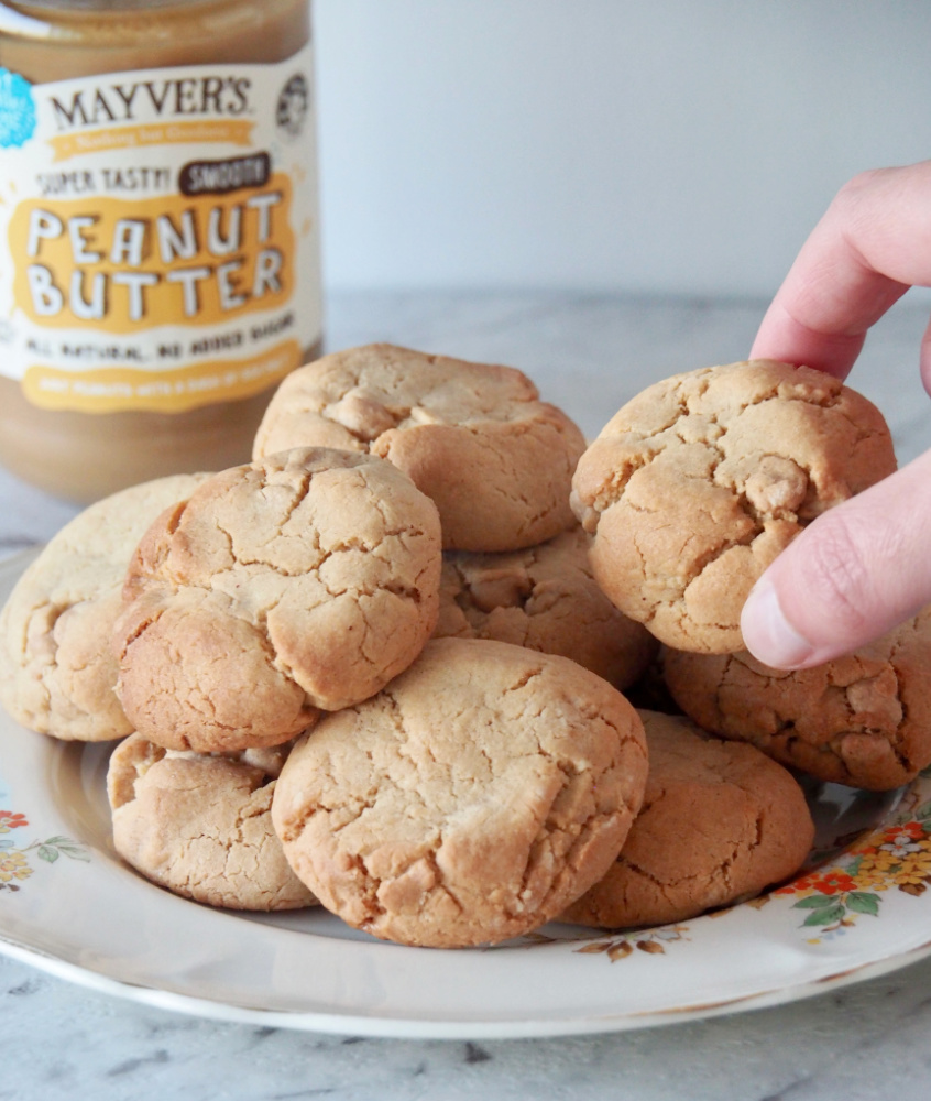 hand taking a peanut butter chip cookie from a vintage plate with jar of peanut butter in background