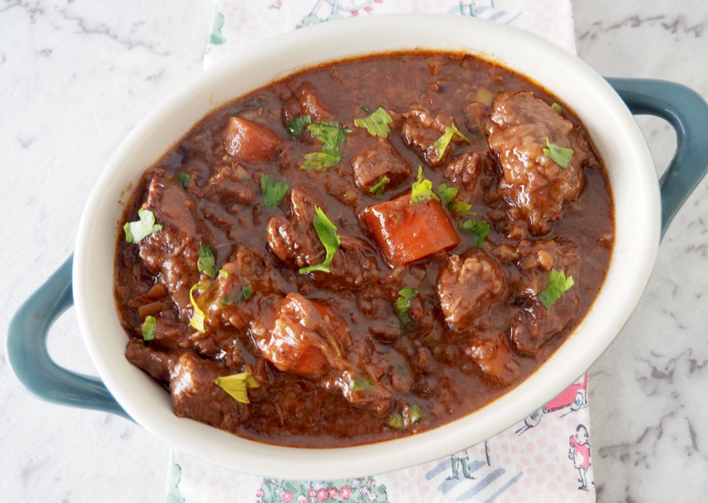 looking down on a pot of beef stew with chunks of beef, thickly sliced carrots and garnished with parsley