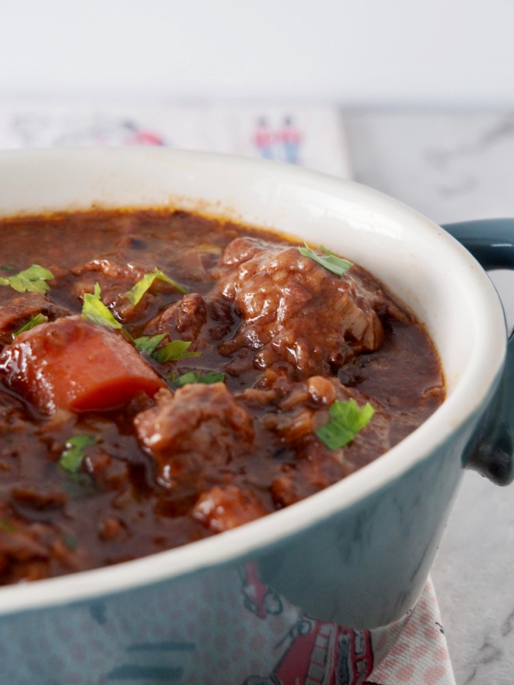 side view of slow cooker beef stew with rich dark gravy, chunks of beef and carrot chunks