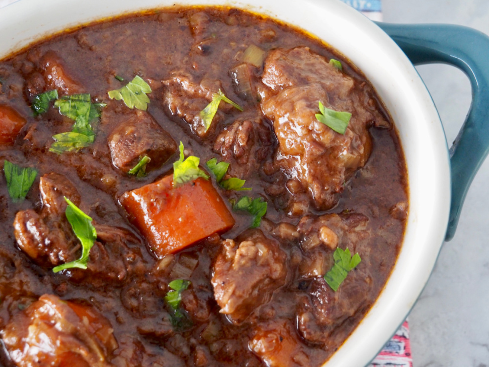 looking down on a pot of beef stew with a rich gravy, chunks of beef, thick carrot slices and garnished with parsley