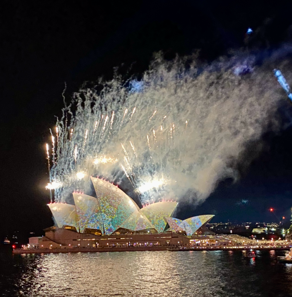 opera house decorated with laser lights with white fireworks shooting off  behind