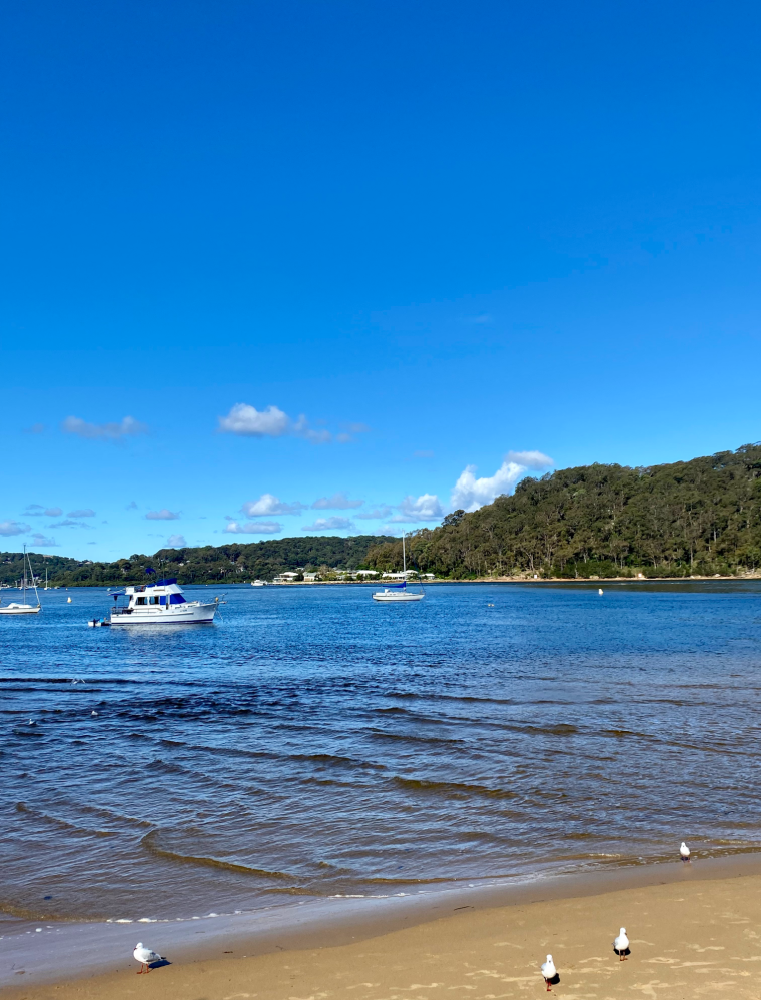 sea at the beach with a few small boats bobbing near to shore. The sky is as deep a blue as the water