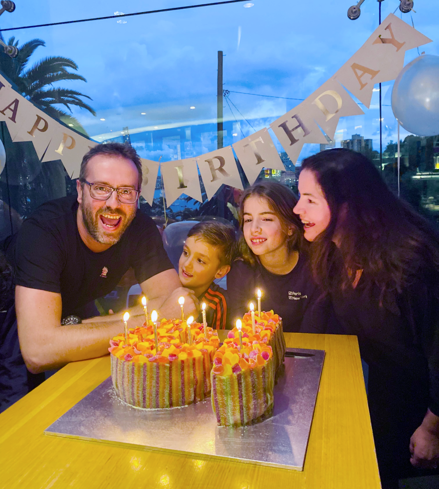 a mum, dad and their two kids are smiling. In front of them is a number 10 birthday cake with 10 lit candles