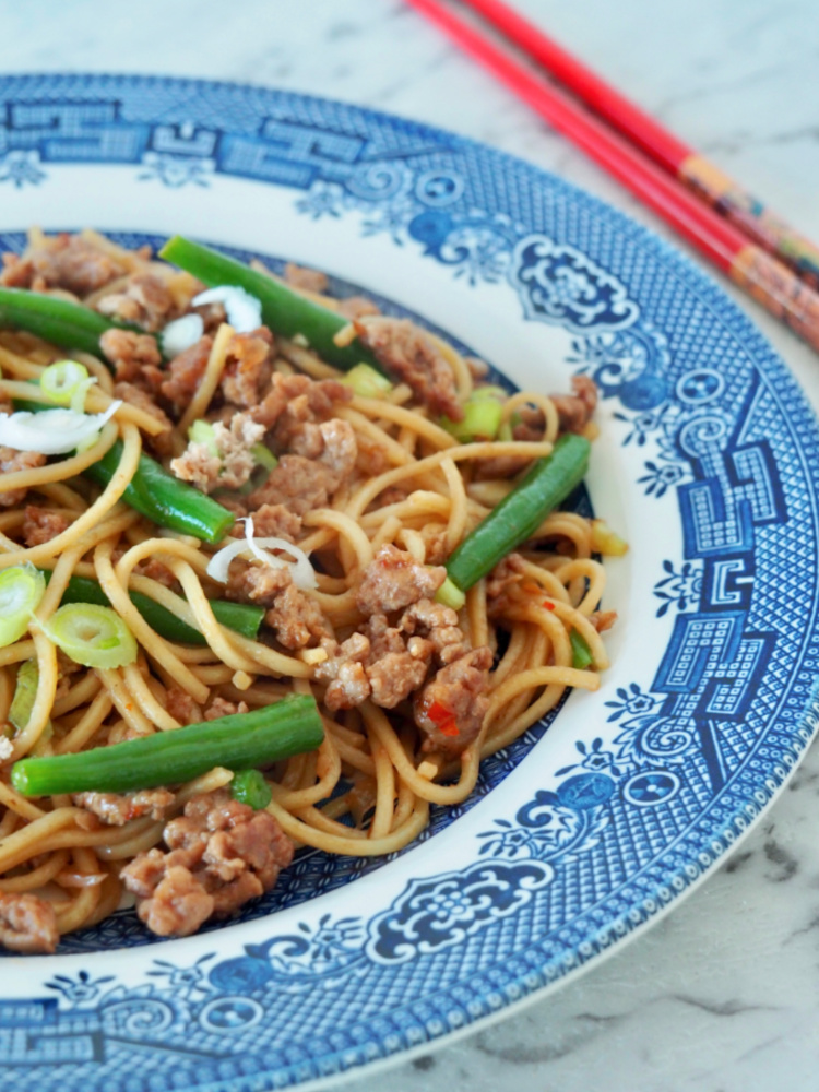 turkey mince noodle stir fry on blue willow pattern plate with red chopsticks to the side