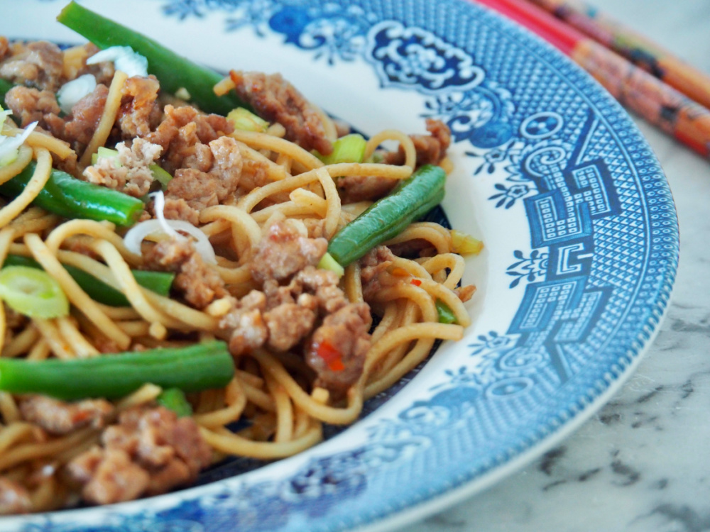 turkey mince noodle stir fry with green beans and garnished with spring onions on blue willow pattern plate
