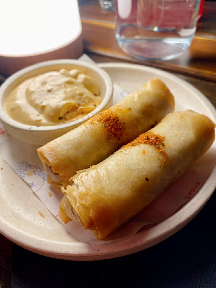 2 cheeseburger spring rolls on a plate with a small pot of aioli