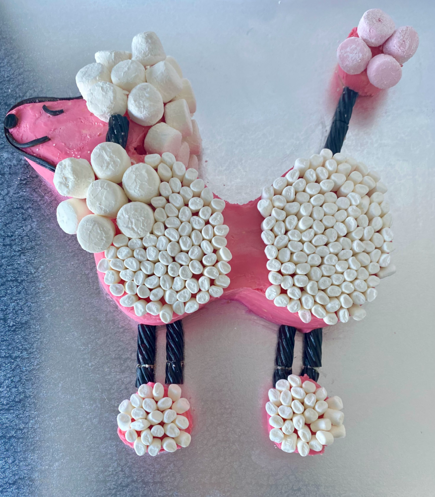 pink birthday cake in the shape of a poodle covered in white marshmallows with licorice legs