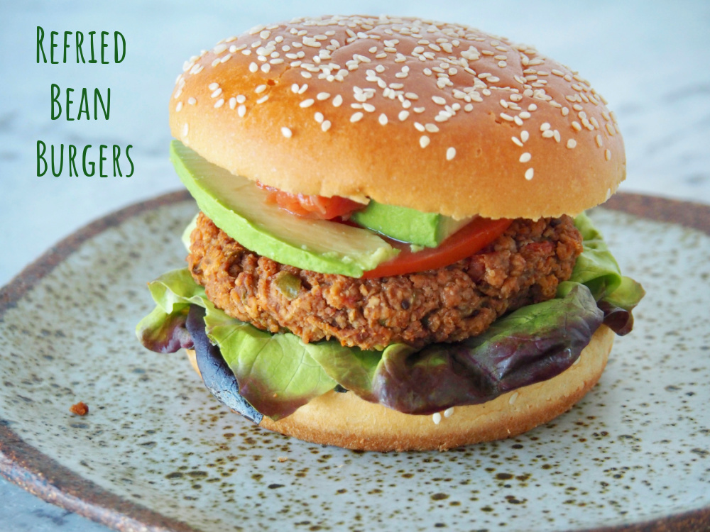 bean burger in a bun with red oak lettuce leaves underneath and sliced avocado and salsa on top