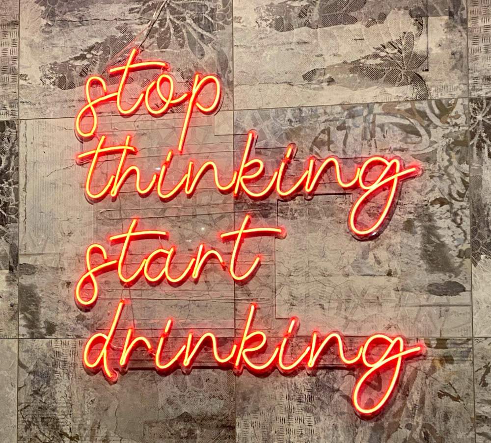 neon sighn against a grey wall that says "stop thinking start drinking"