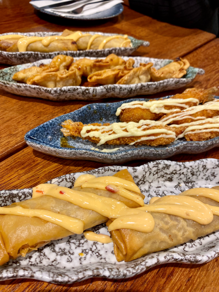 selection of small plates on table with spring rolls drizzled with cheeseburger sauce in the foreground