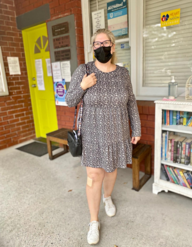 woman wearing a black leopard print dress, white sneakers and a black face mask standing outside a doctor's surgery