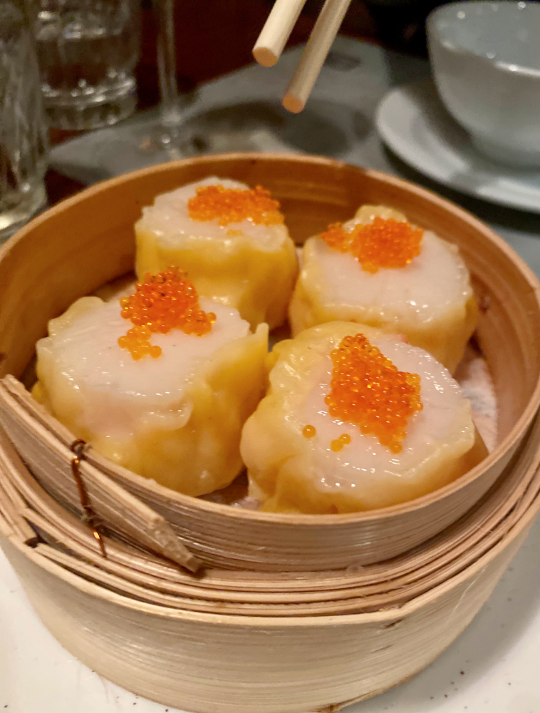 a pair of chopsticks hovering over a bamboo steamer of siu mai dumplings