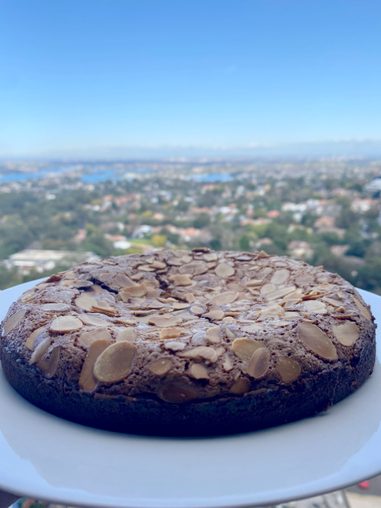 a plate with a flourless coconut and almond cake against a background of blue skies and city views