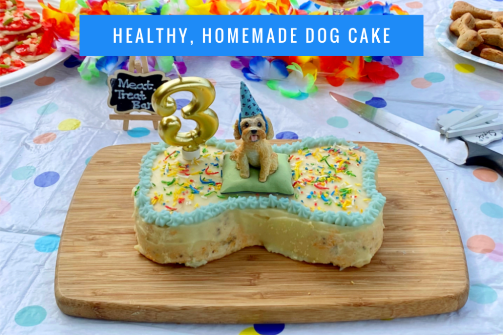 a bone shaped cake with blue piped icing around the edge, coloured sprinkles and a clay modelled cavoodle cake topper.
