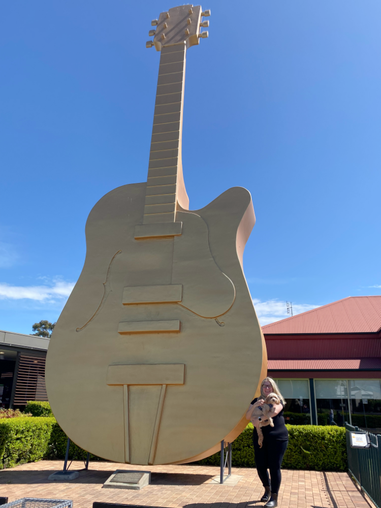 a woman holding a small dog in front of the big golden guitar in Tamworth