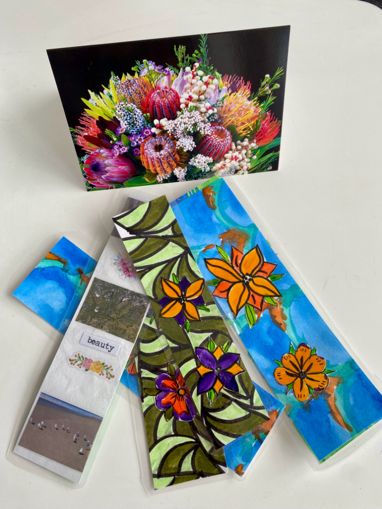 4 colourful bookmarks laid out on a table in front of a greeting card with a picture of flowers on it