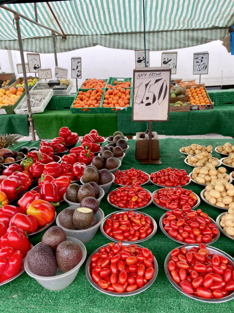 a market stall with rows of bowls filled with produce. A sign says "all bowls £1.50"