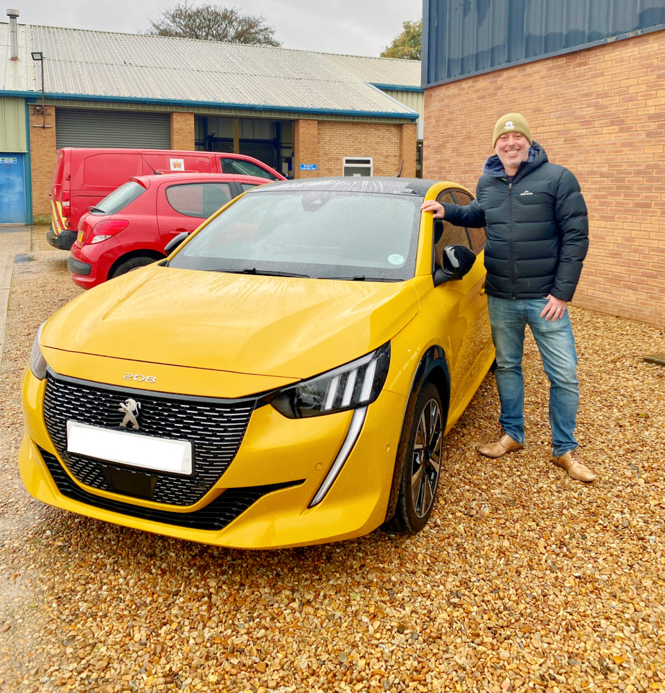 a man wearing a beanie and a black puffer jacket standing next to a yellow peugeot 208