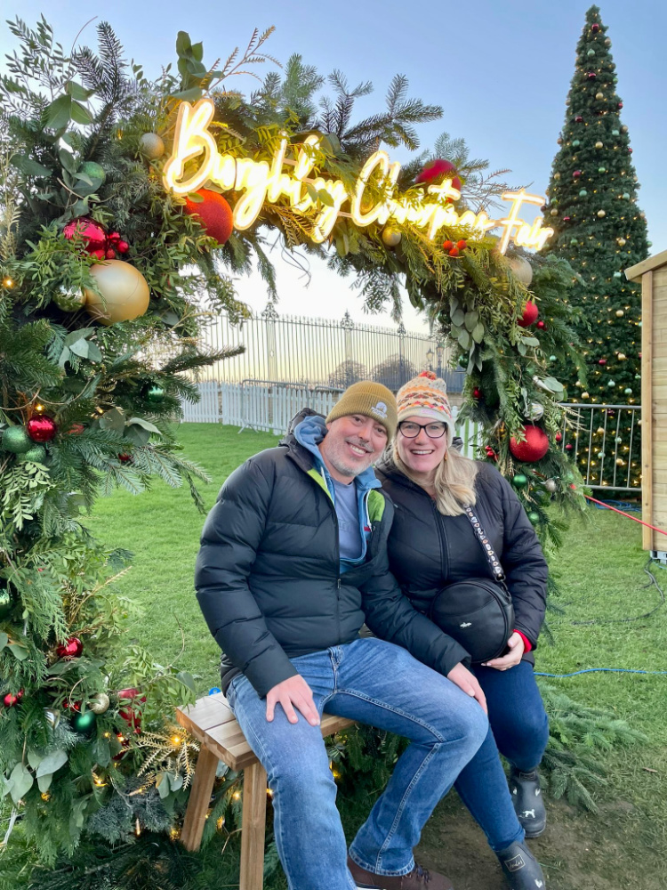 a man and woman smiling sitting under a wreath arch and a neon sign that says Burghley Christmas Fayre