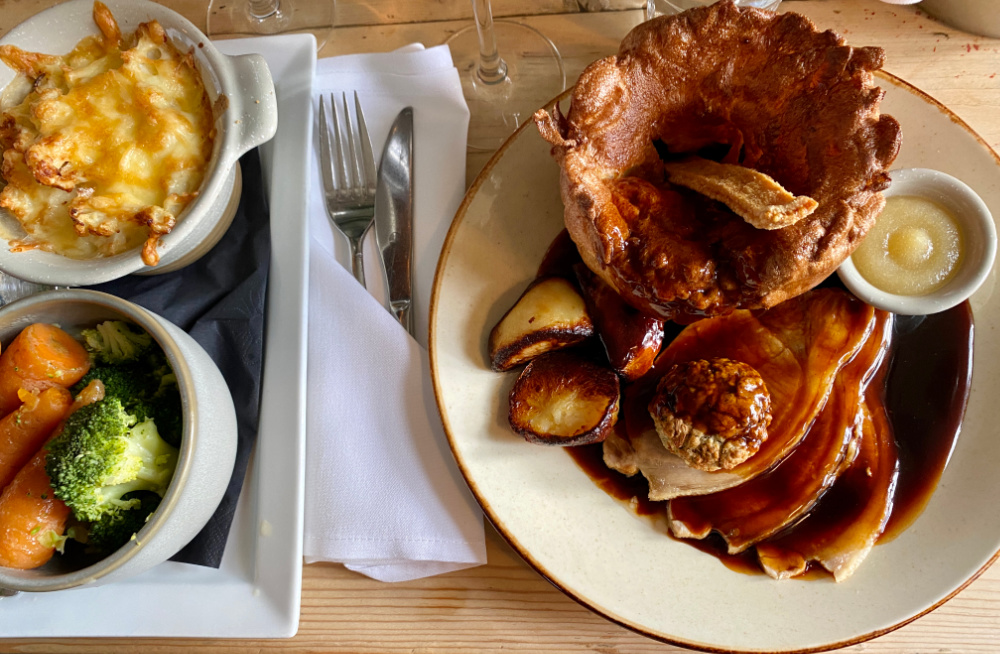 a plate of sunday lunch - meat with roast potatoes, gravy and a giant yorkshire pudding