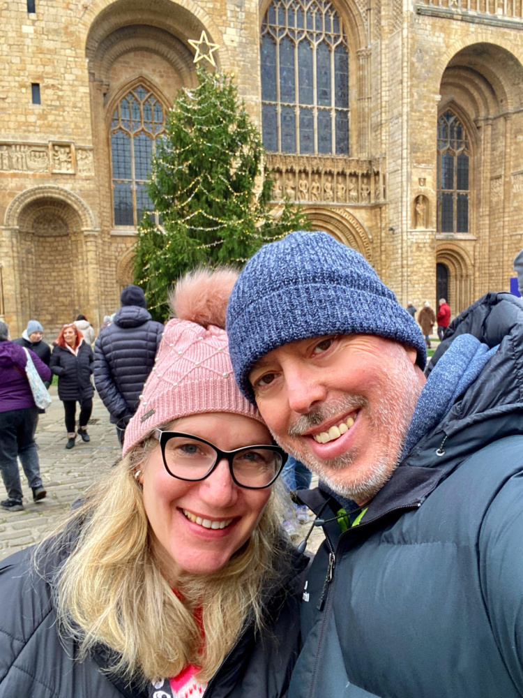 a man and woman wearing beanies and smiling in front of Lincoln cathedral