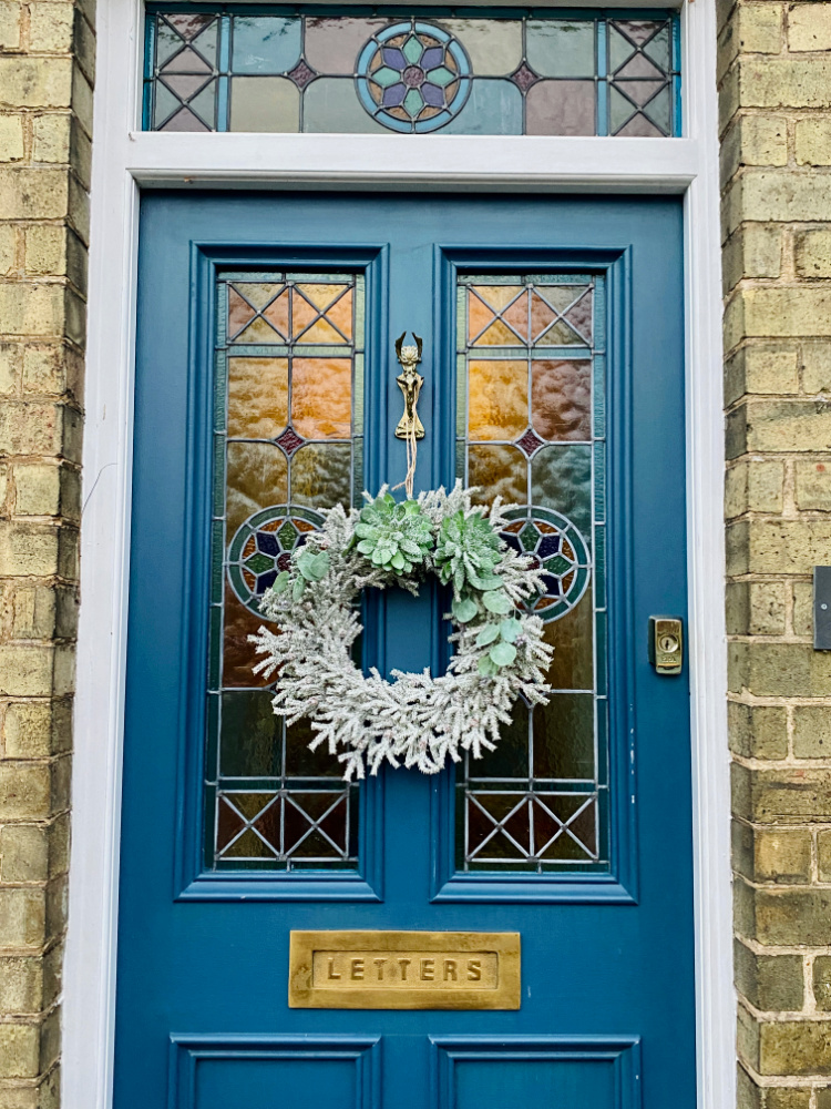 a snow dusted succulent wreath hanging on a blue front door with stained glass window panes