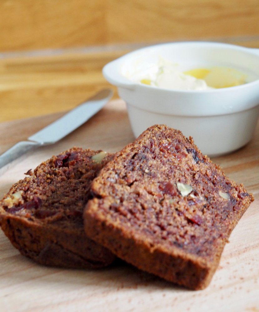 two slices of persimmon loaf stacked on a board with a small bowl of butter in the background