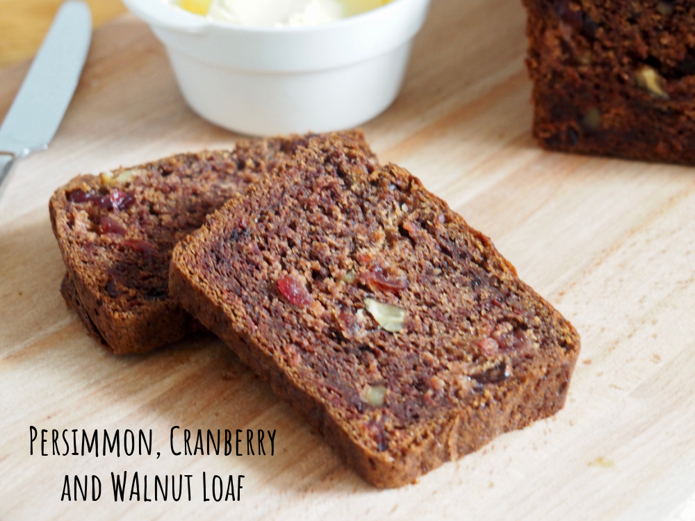 slices of persimmon, cranberry and walnut loaf on a board with small bowl of white butter in background