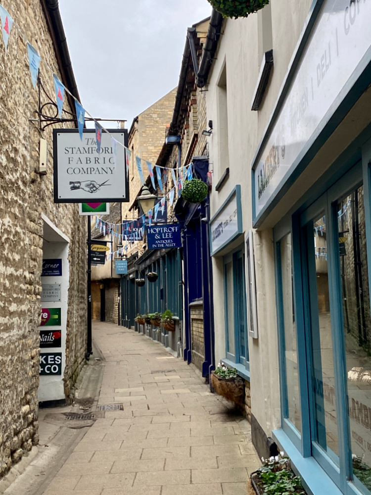 looking down a narrow lane with old shops and hanging signs