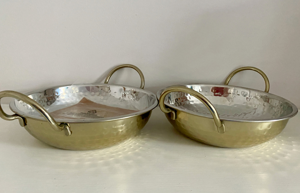 two golden balti dishes side by side on a white shelf