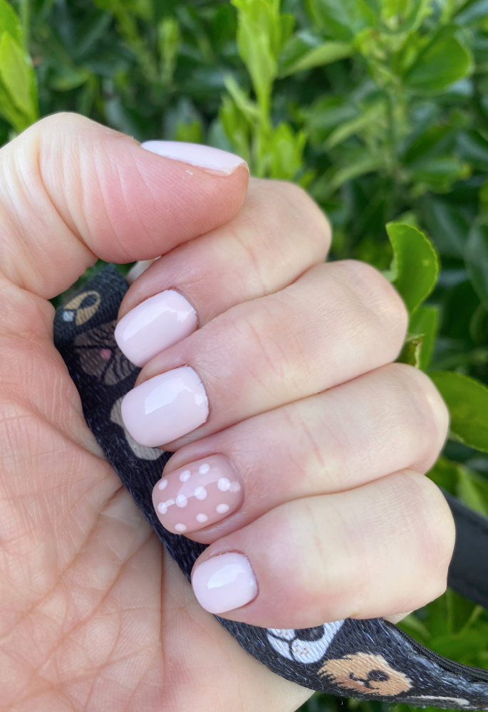 hand showing fresh manicure with 4 baby pink nails and baby pink polka dots on the ring finger nail