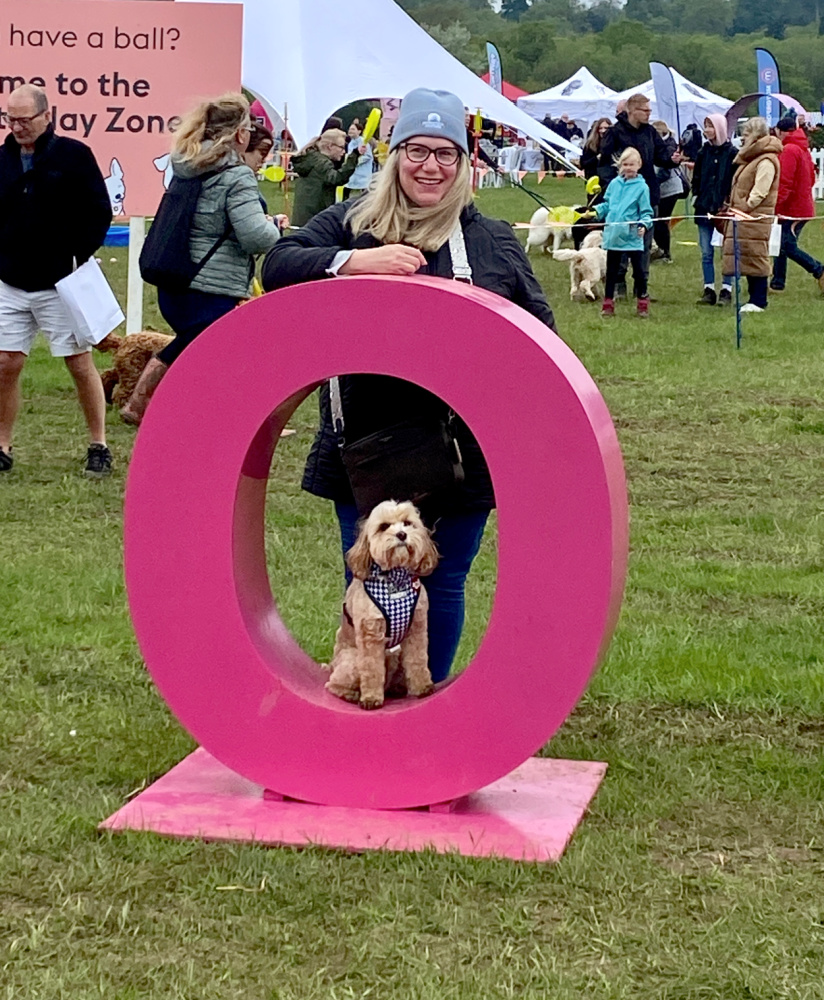 a dog sitting in the middle of a large pink letter O and a woman standing behind leaning on the top of the letter