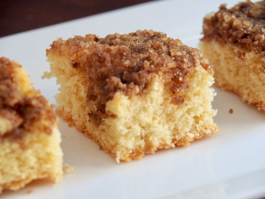 close up of a square of sponge topped with crunchy walnut topping on a white rectangular plate