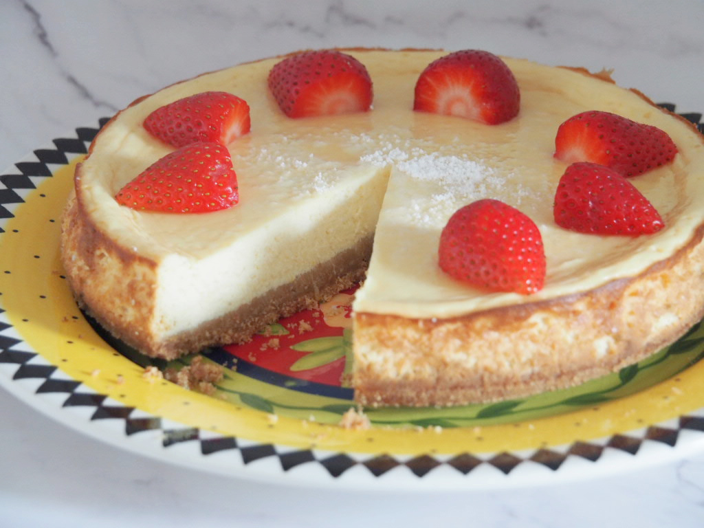 whole lemon cheesecake with one slice removed. The cheesecake is decorated with halved strawberries.